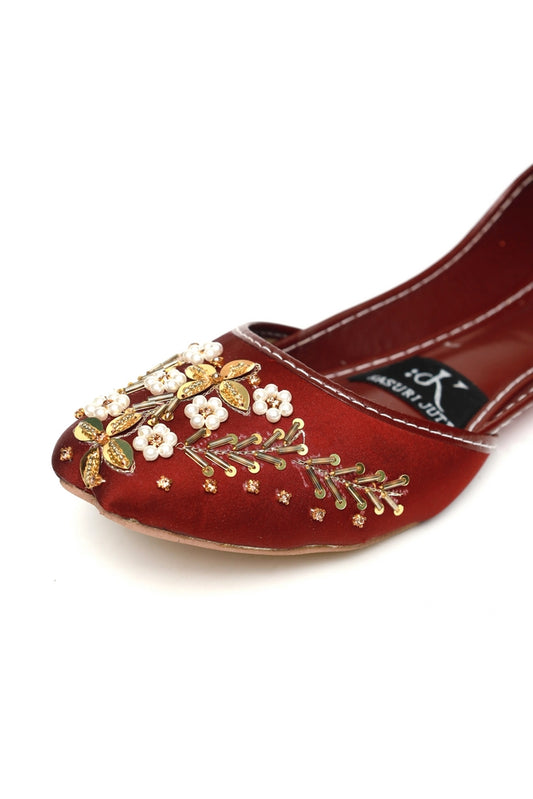 Close-up of red maroon Kasuri Jutti with intricate gold zari, pearl, and floral embroidery on toe
