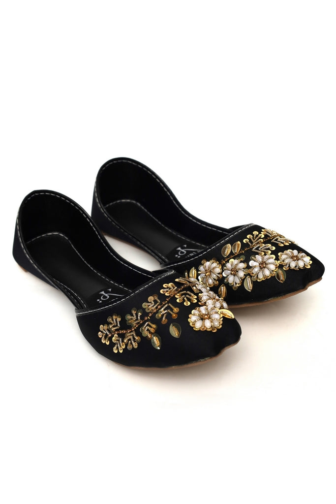 Black flats kasuri jutti with gold and pearl embellishments on a white background