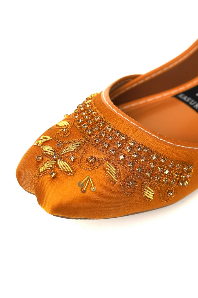 Close up of orange-yellow kasuri shoe with gold embroidery on a white background